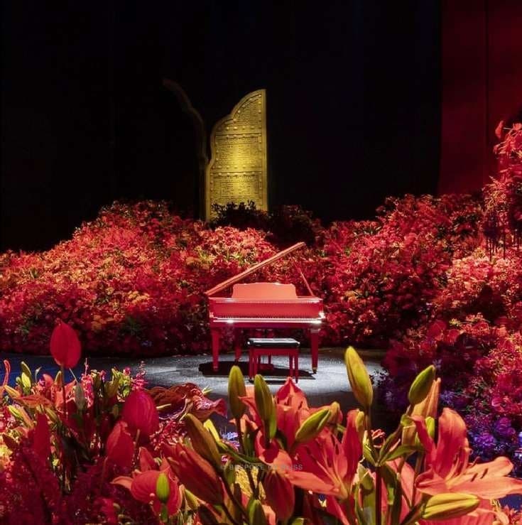 A red piano on a stage surrounded by red flowers