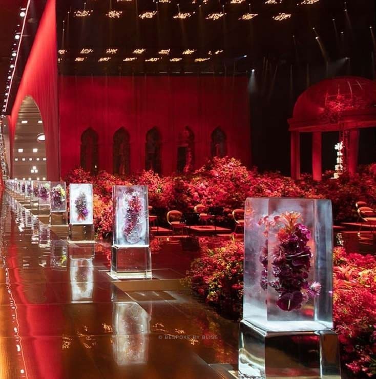 A long red hall with flowers set inside blocks of ice beside a floral landscape