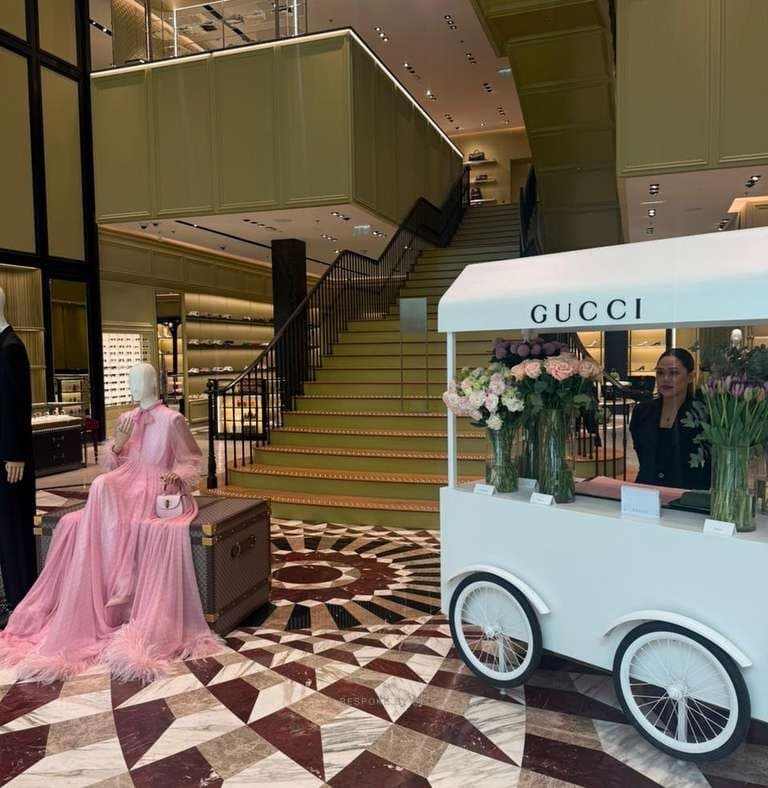 A white floral cart with roses and tulips in glass vases beside a staircase