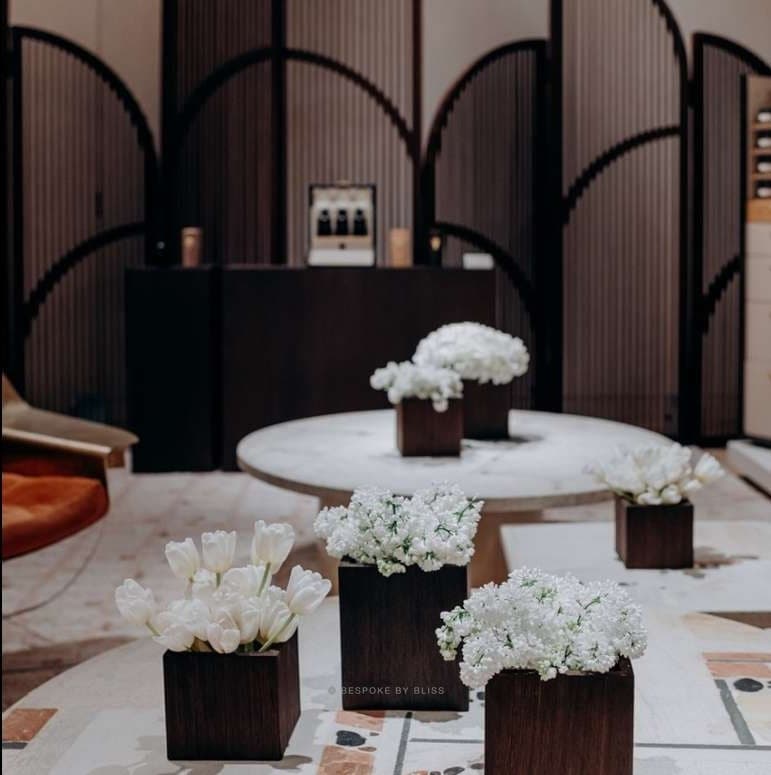 White flowers in wooden boxes on a low table in front of an arched screen