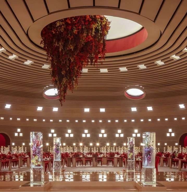 A hanging red floral installation above set tables in a round hall