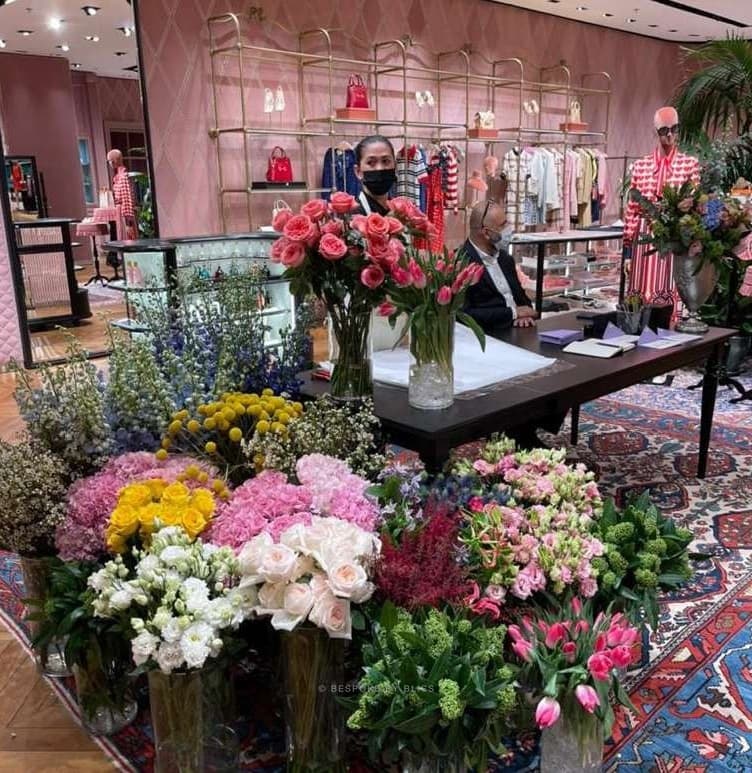 Fresh flowers in glass vases on the floor of a boutique, with staff at a desk behind