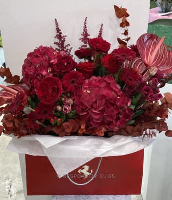 A deep red flower arrangement in a red paper bag