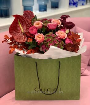 A red and coral bouquet in a green patterned paper bag on a pink sofa