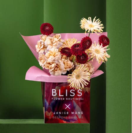 A bouquet in pink wrapping above a red branded gift carrier in a green niche