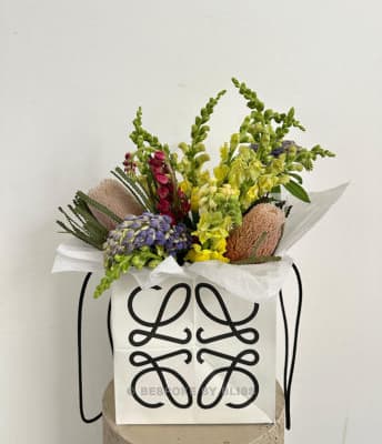 A bouquet of wild flowers rising from a white paper bag printed with a monogram