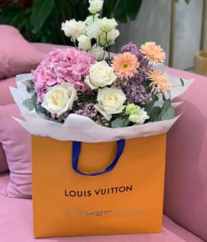 White and pink flowers in an orange paper bag on a pink sofa