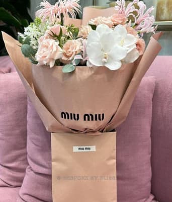 A peach-wrapped bouquet with white orchids above a paper bag