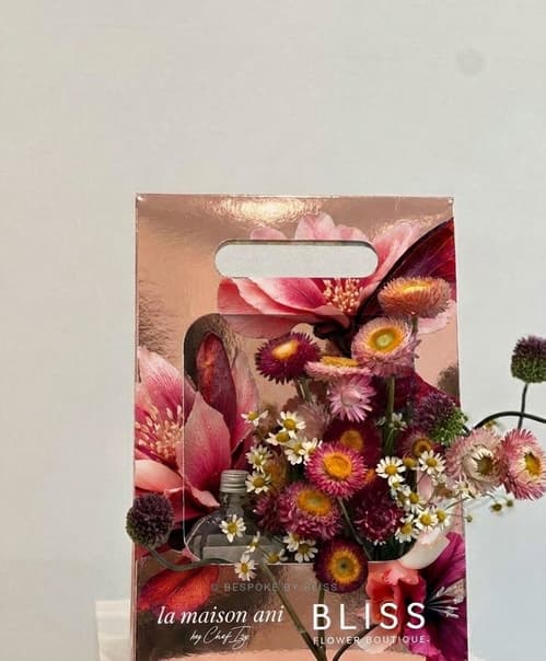 A branded gift carrier with printed artwork holding dried and fresh flowers